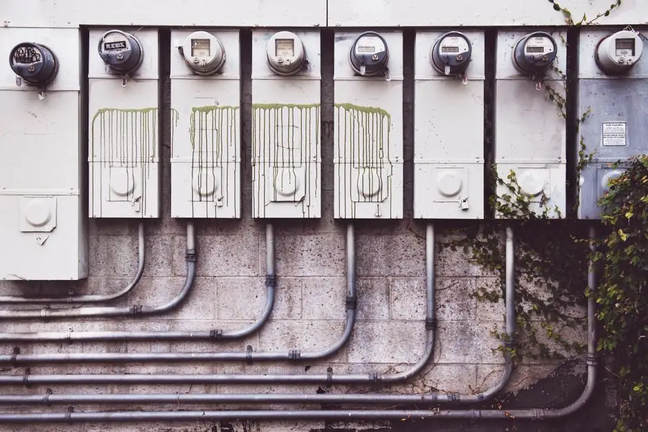 Array of outdoor electric meters on a brick wall with vines.